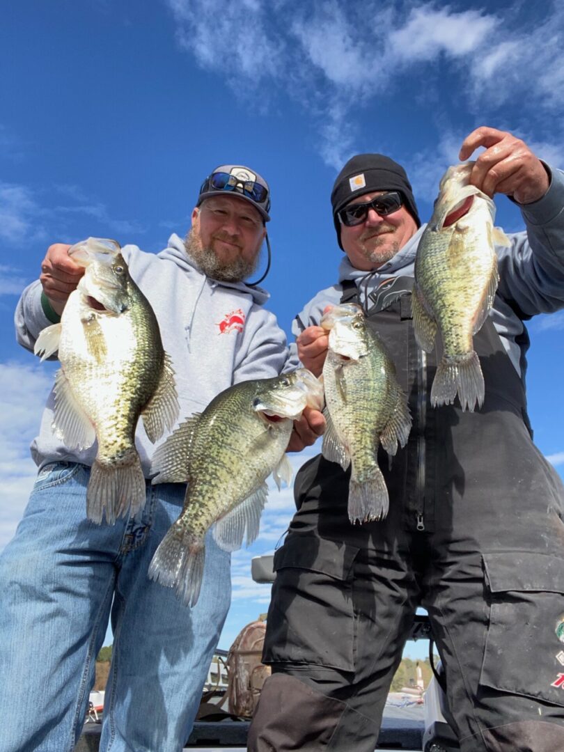 Two men holding up fish while standing on a beach.